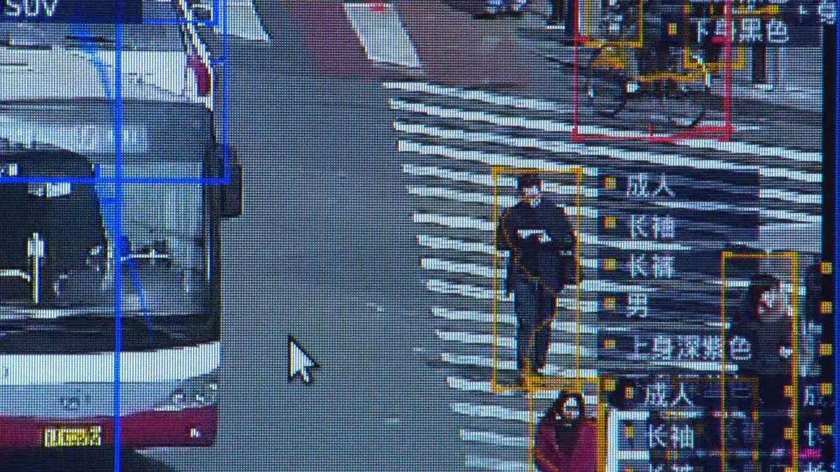 Man crossing a street at a crosswalk as seen from a surveillance camera.