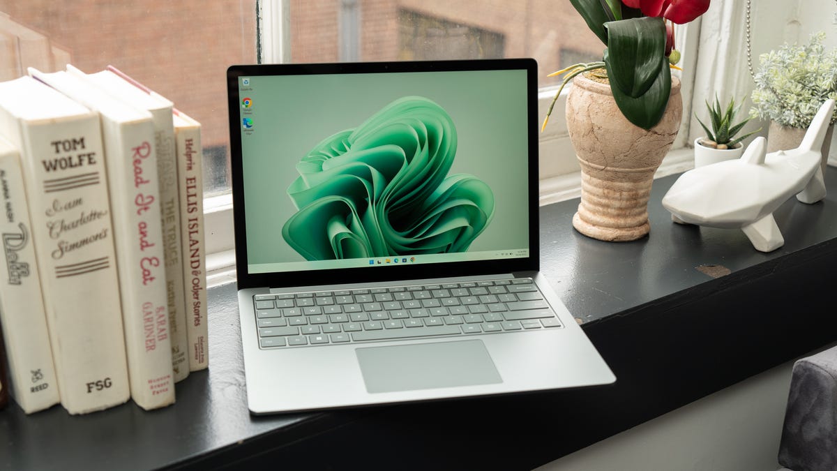 Sage green Surface Laptop 5 open and sitting on a black windowsill with books to its right