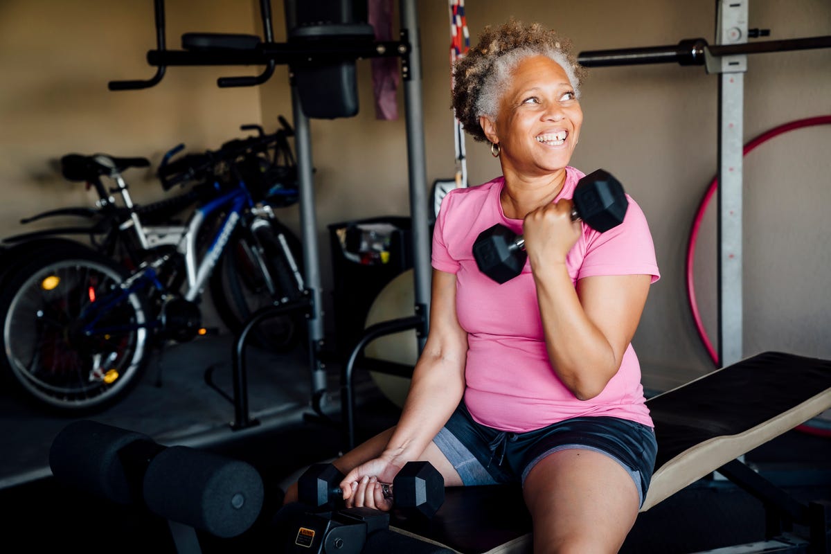 Smiling woman lifts dumbbells in garage.