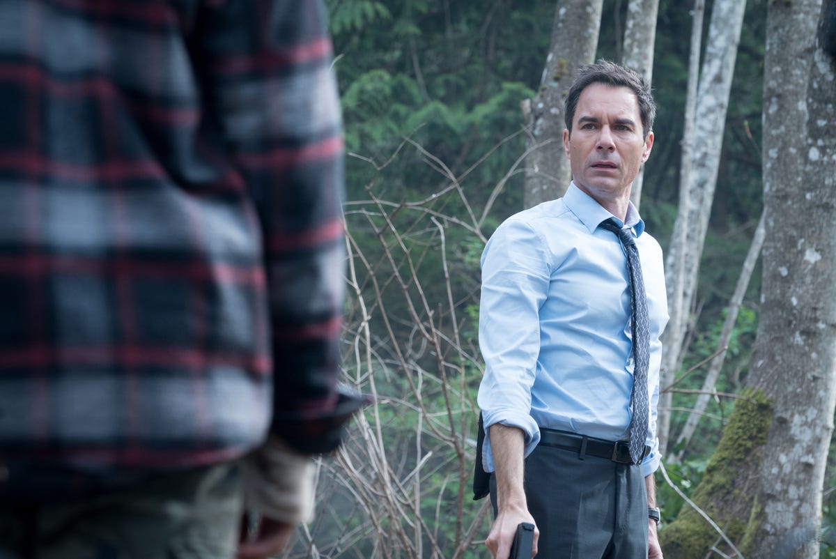 Eric McCormack as an FBI agent has a gun in his hand in the woods