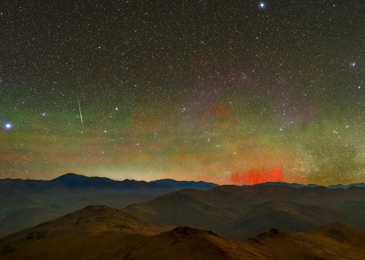 Painterly landscape of mountains and star-studded night sky with a glowing red brush-like lightning phenomenon.