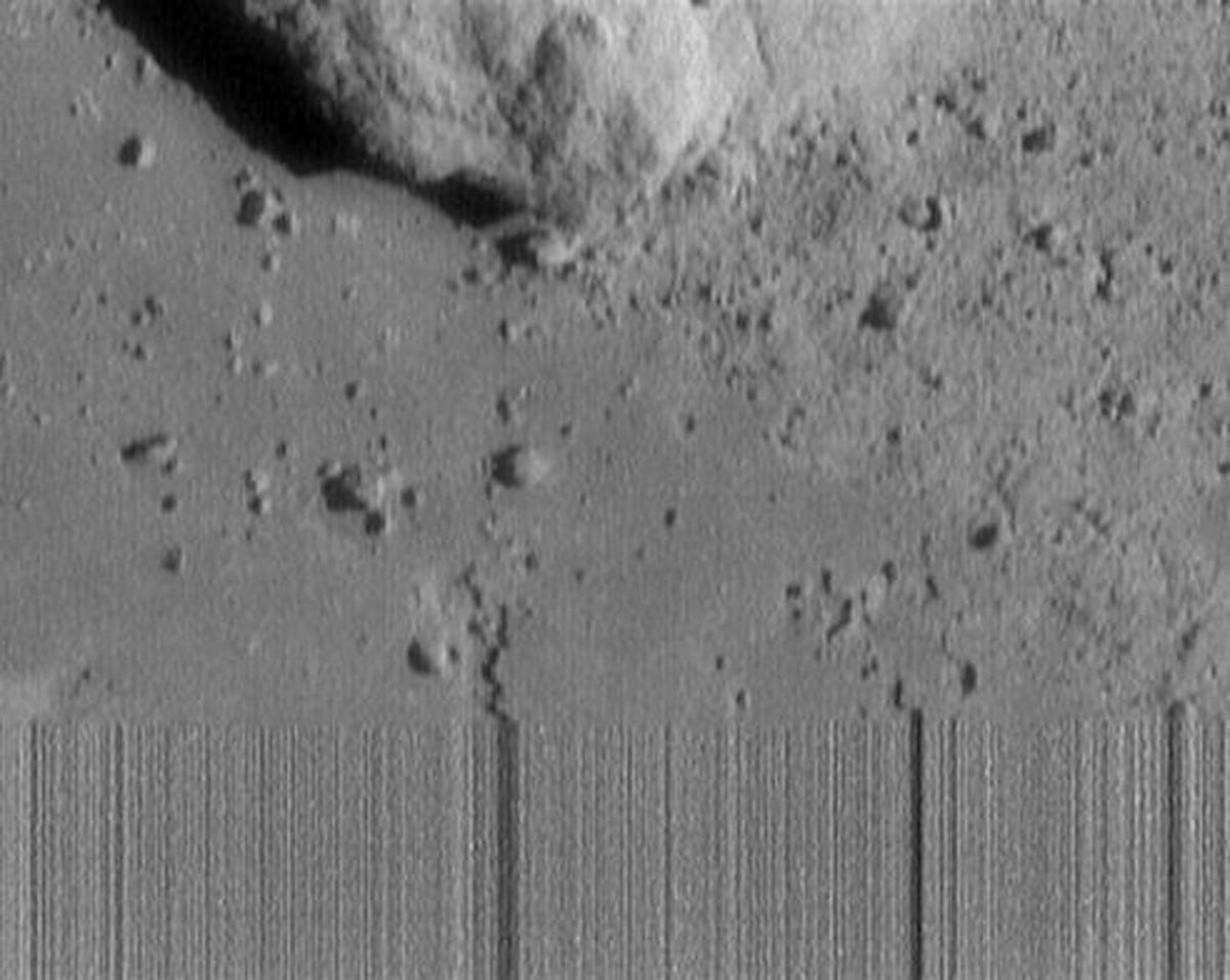 Blurred out section at the bottom of a very gray image showing a rocky and lumpy asteroid.