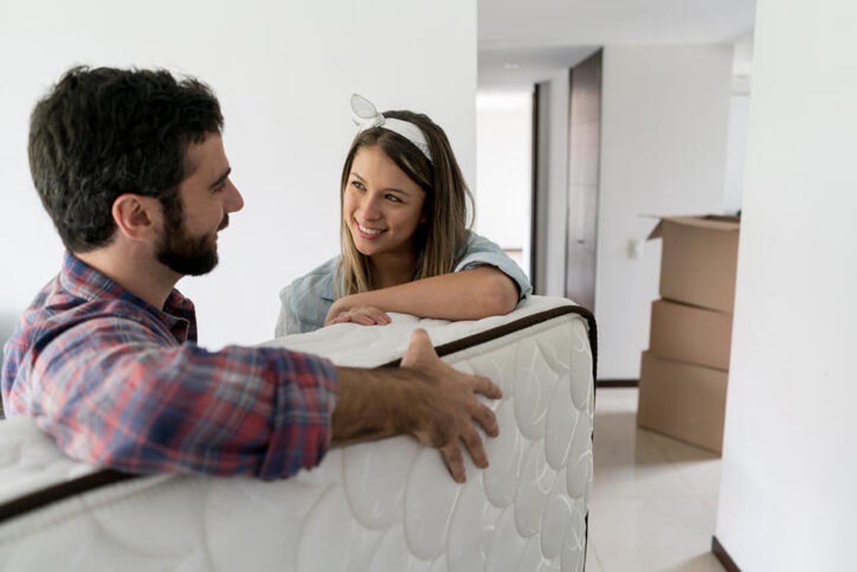 Man and woman talking while moving a queen-sized mattress.