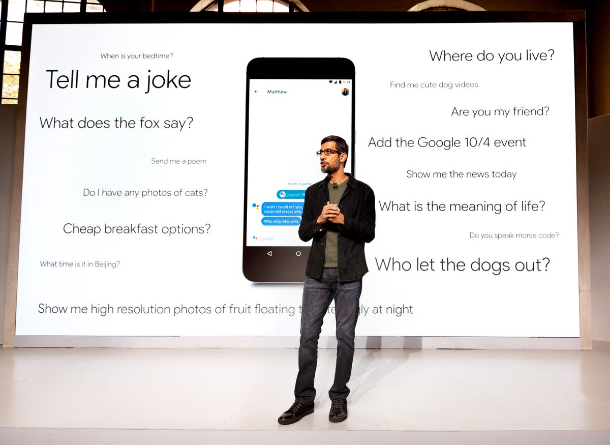 ​Google CEO Sundar Pichai stands before queries you can ask Google Assistant.