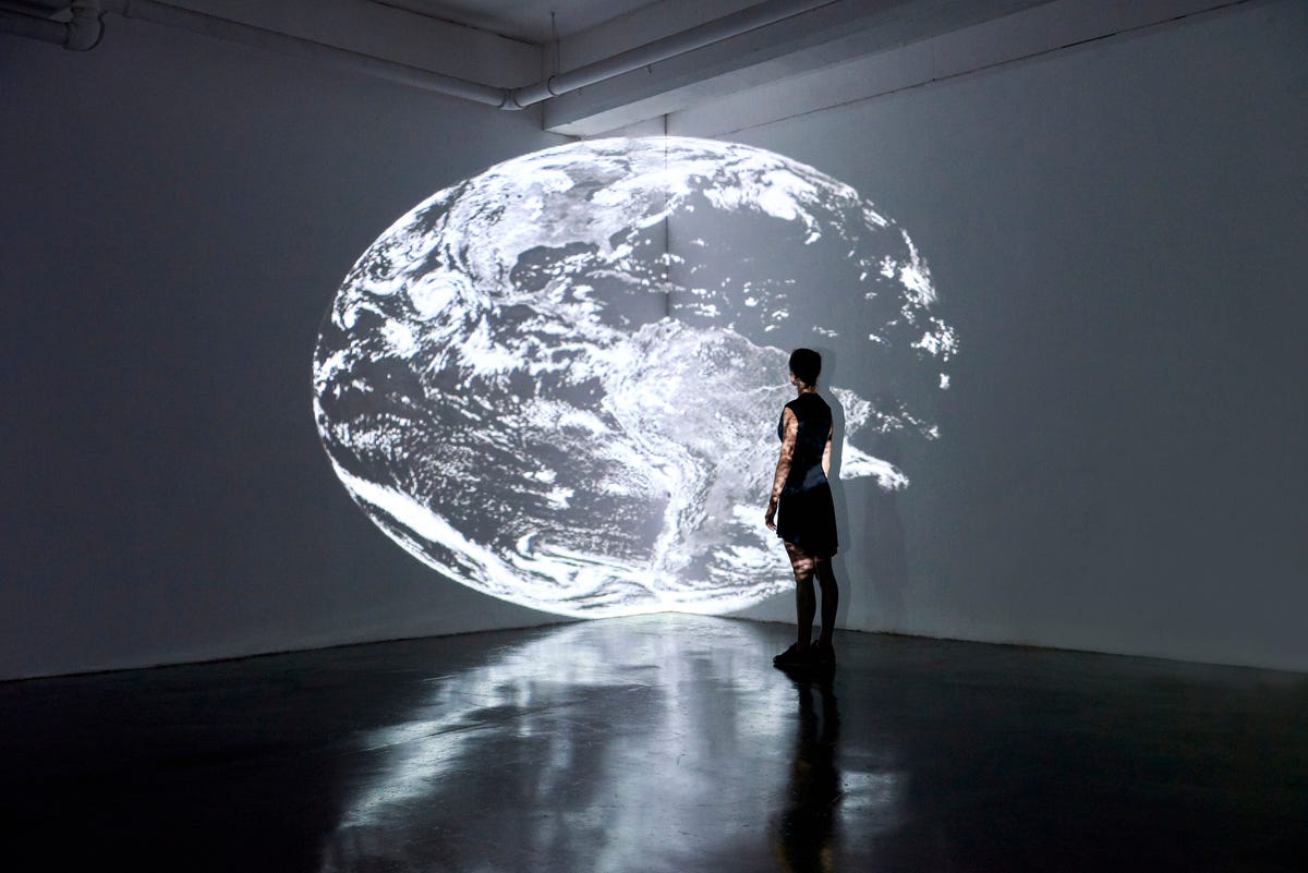 Person stands in gallery watching a projection of the Earth.