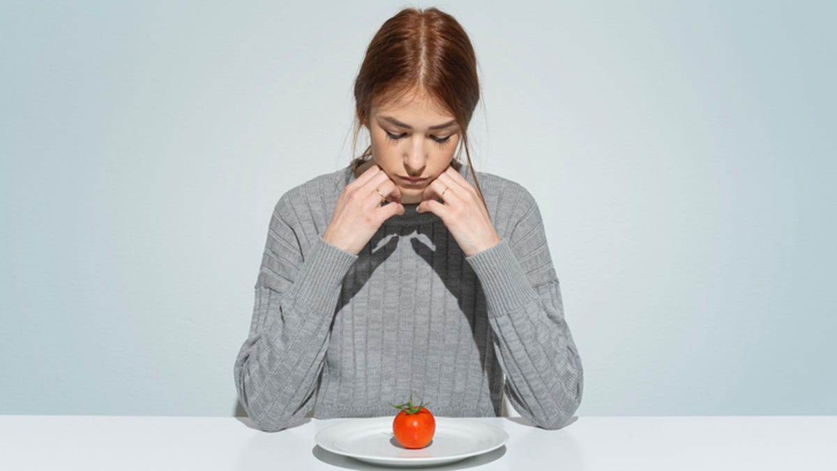 Young woman staring down at a plate with a tomato on it, depicting an eating disorder.