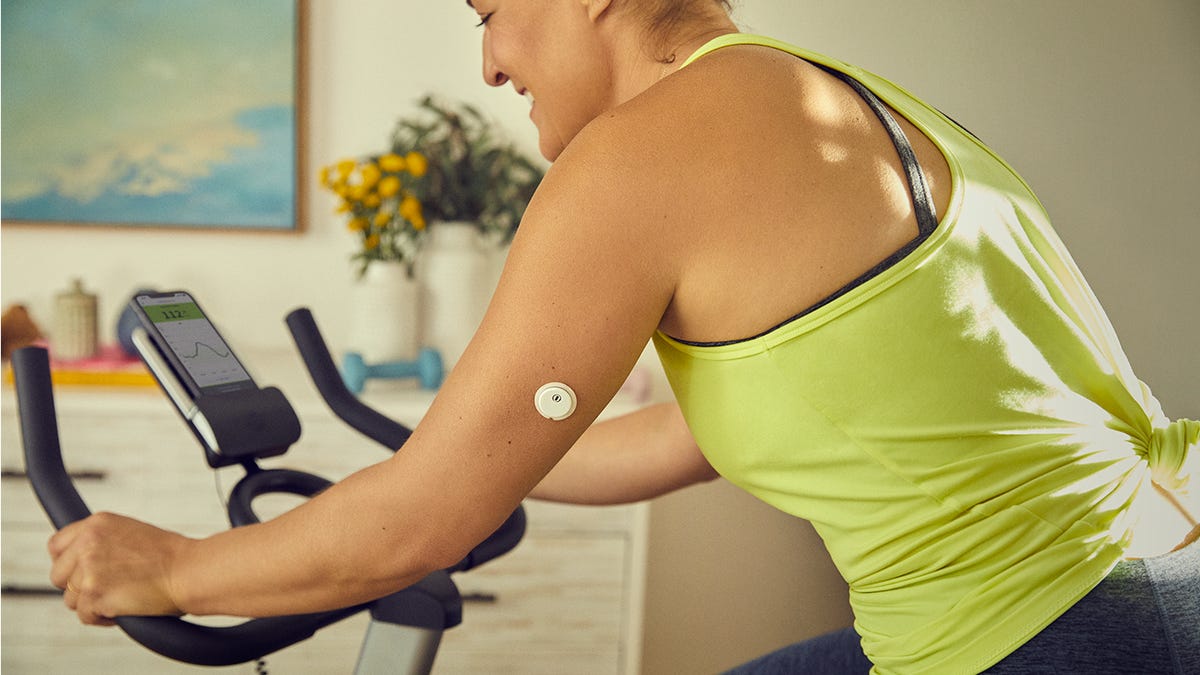A person riding an exercise bike with a small white circular sensor attached to their arm