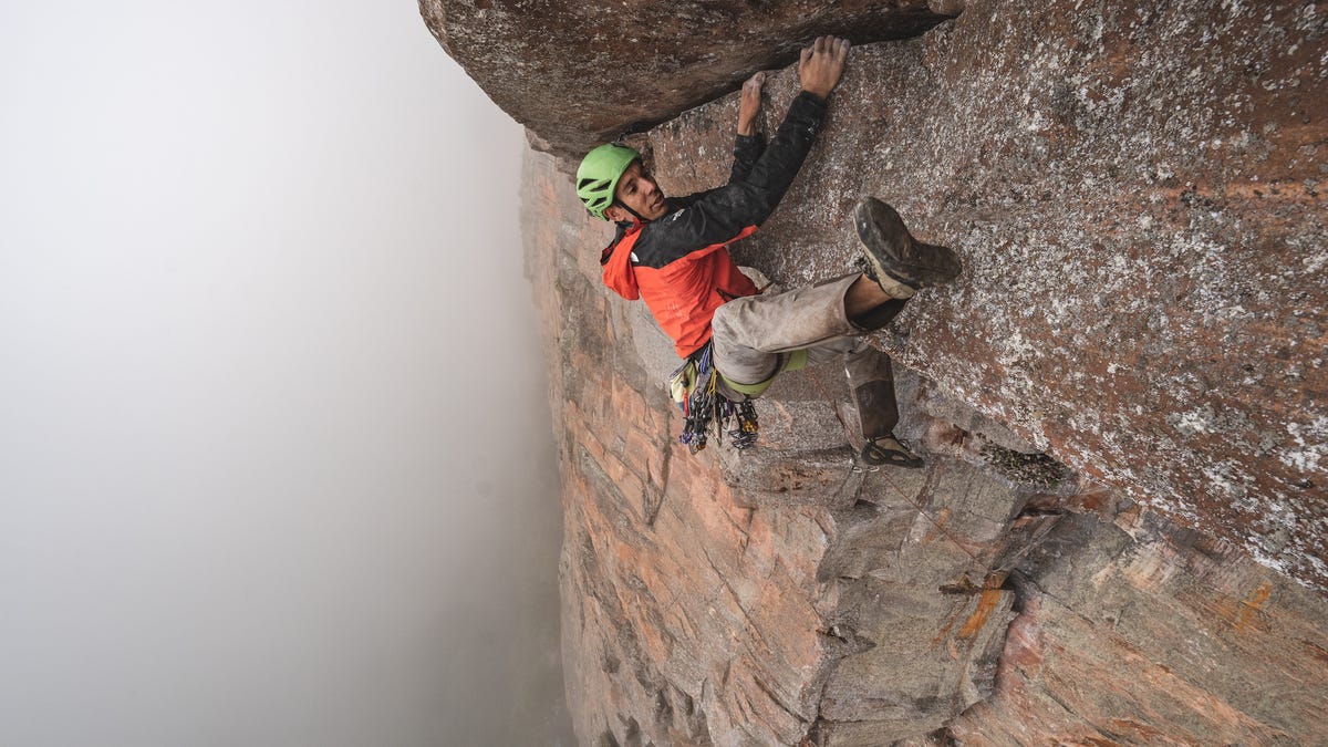 Alex Honnold, star climber of Free Solo, is shown clinging to the tepui's sheer rock wall with heavy mist blotting out the jungle below.