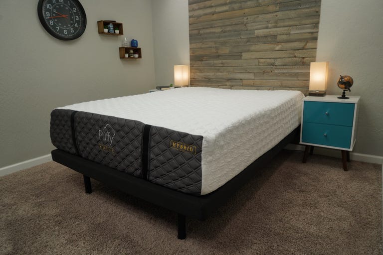 A Puffy Royal mattress sitting on top of a black bed frame inside of a well-lit room.