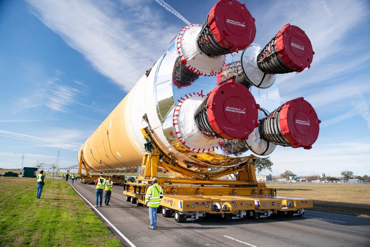 The core stage of the Artemis I rocket is rolled horizontally down a road from the Michoud Assembly Facility, ready to be loaded onto a barge.