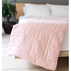 Pink Baloo The Mini Weighted Blanket draped over the edge of a bed