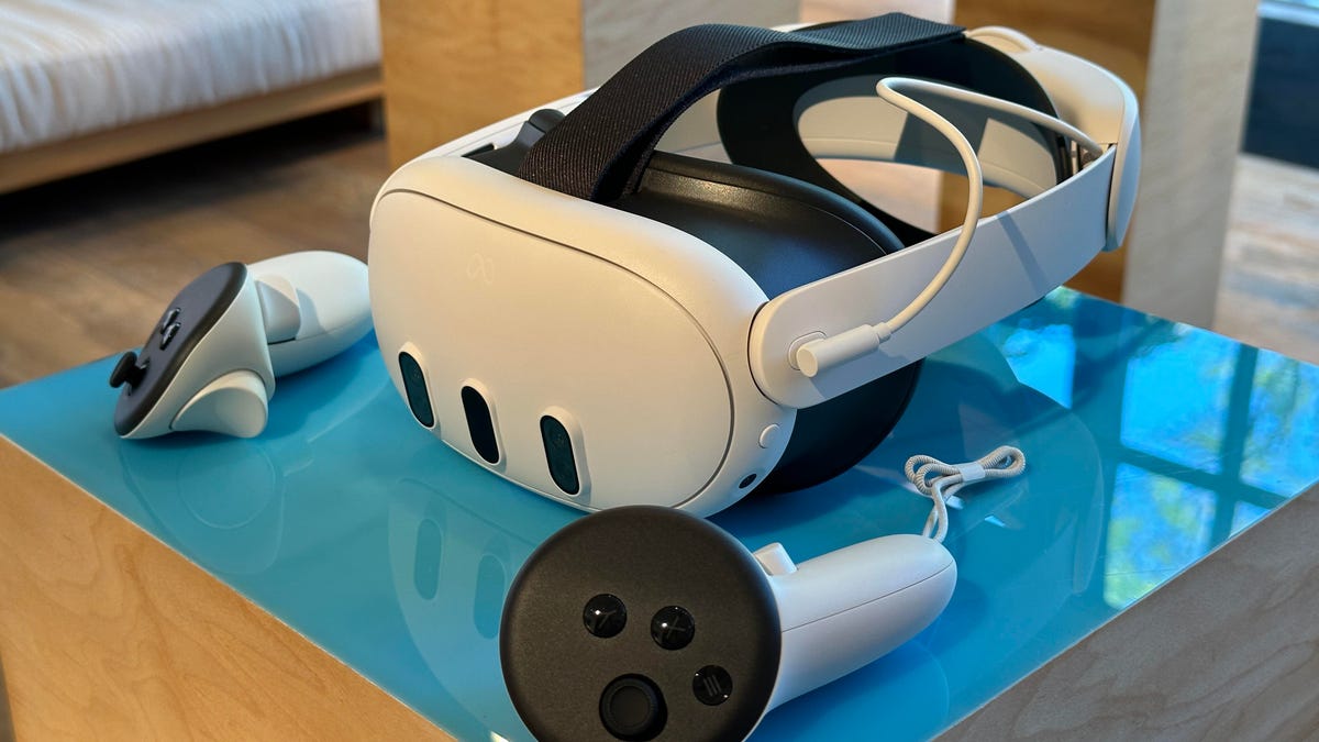 A Quest 3 on a table in white, a VR headset with a wired battery pack head strap and controllers