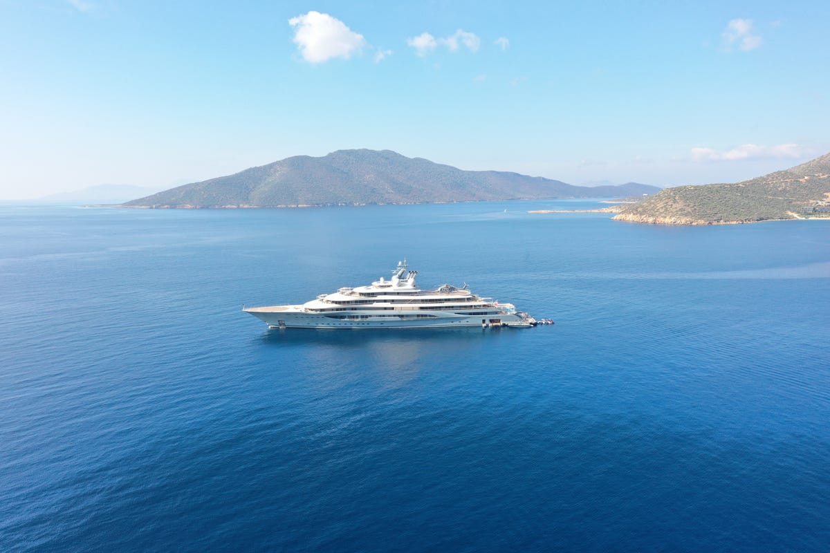 A large yacht in open water with a coastline in the background