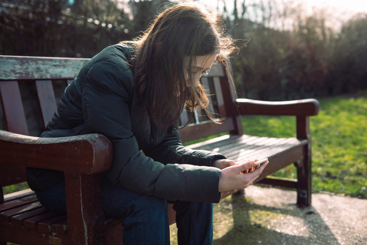 Girl sitting on a park bench looking at a phone