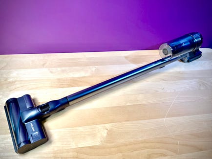 The Samsung Jet 90 cordless vacuum cleaner lays flat atop a hardwood floor beside a magenta-colored wall.