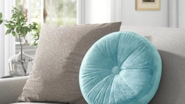 A teal round pillow sitting on a couch alongside a square pillow