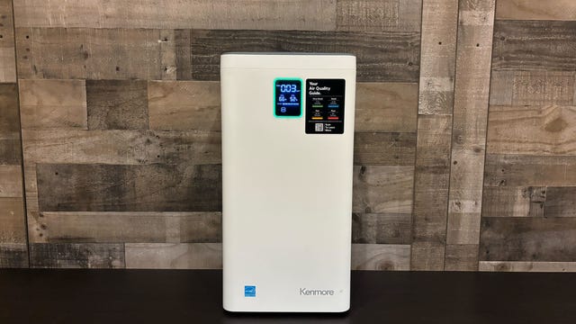 The Kenmore Smart 2300e Air Purifier sits on a table in front of a wooden wall.