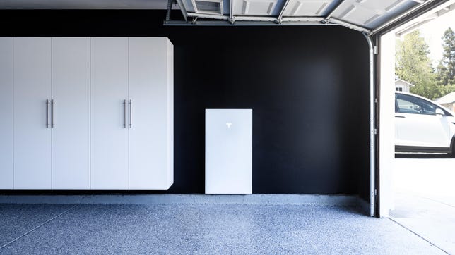A white Powerwall 3 battery next to white cabinets in a garage with an open door.