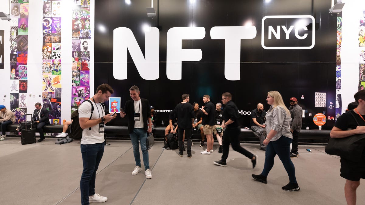 Convention goers standing, sitting and walking in front of a wall-size NFT.NYC sign