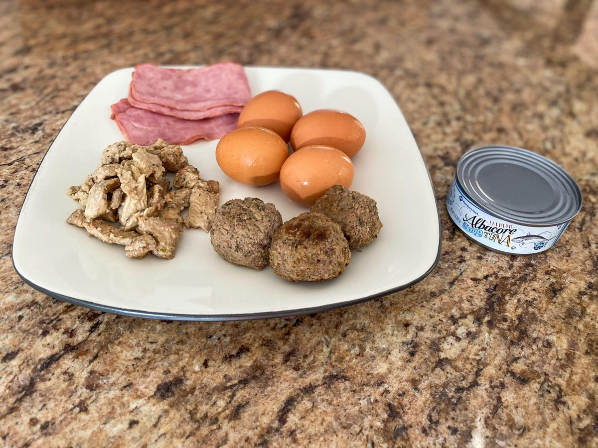 A spread of food containing turkey, ham, eggs, tuna, and beef depicting 100 grams of protein