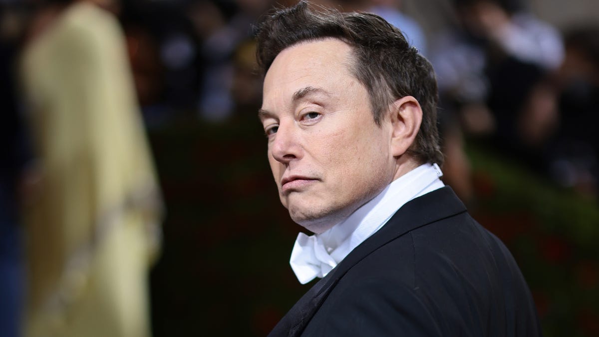 elon musk, dressed in a tuxedo, glances over his shoulder