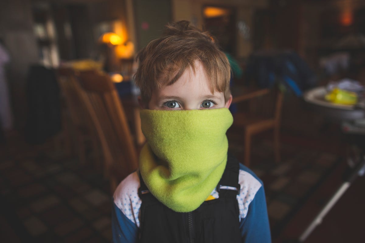 Child wears a green scarf over mouth.
