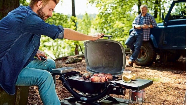 A man cooks meat on a grill in the woods