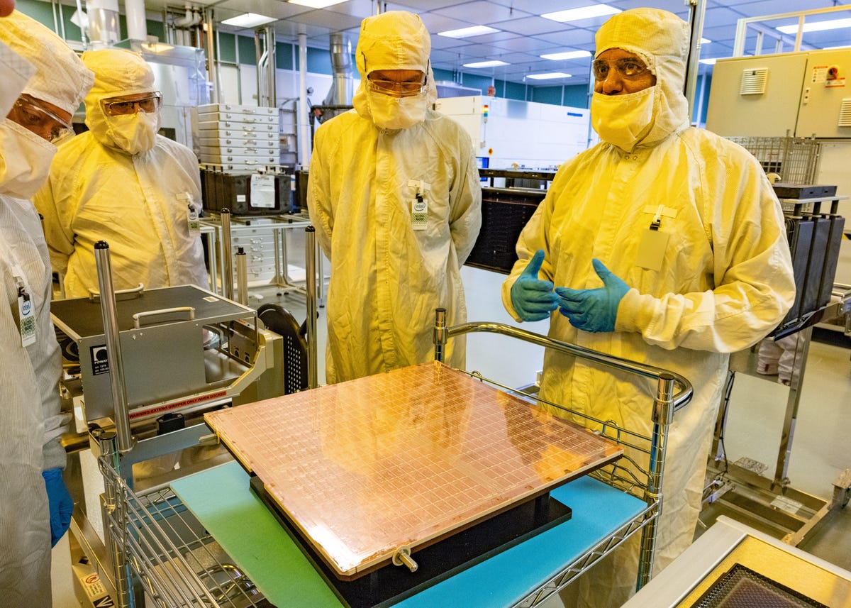 Rahul Manepalli, right, Intel's module engineering leader, shows a glass substrate panel before it's sliced into the small rectangles that will be bonded to the undersides of hundreds of test processors. The technology, shown here at Intel's CH8 facility in Chandler, Arizona, stands to improve performance and power consumption of advanced processors arriving later this decade. Glass substrates should permit physically larger processors comprised of several small "chiplets" for AI and data center work, but Intel expects they'll trickle down to PCs, too.