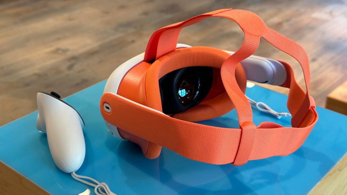 A white VR headset with an orange faceplate and head strap, sitting on a blue mat on a table