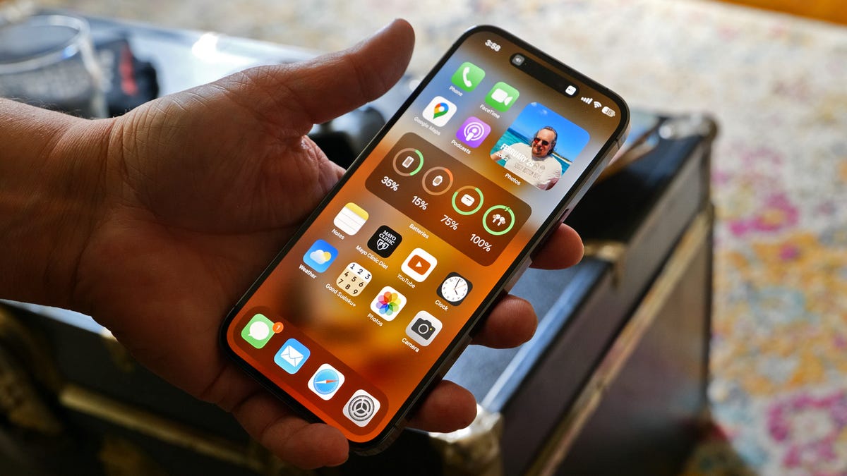 Hand holding the iPhone 14 Pro Max with the home screen active