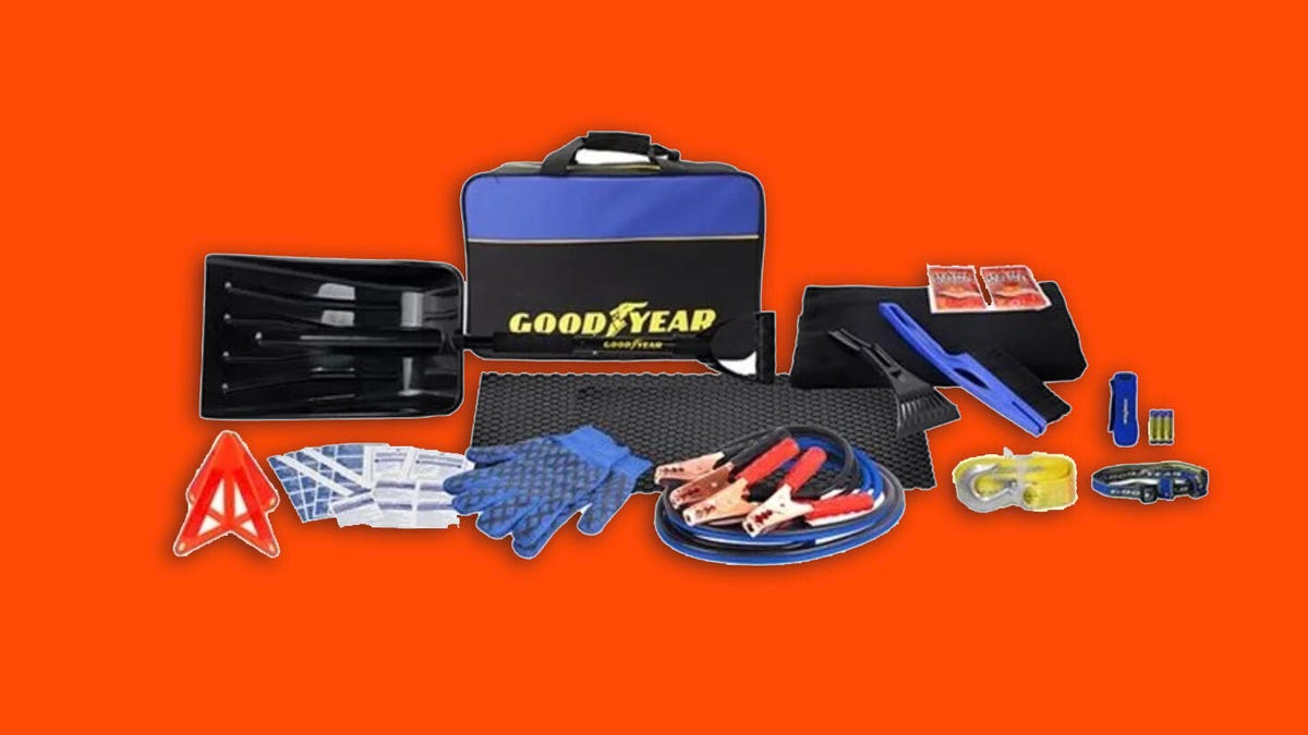 The contents of a Goodyear emergency kit, including jumper cables, a pair of gloves, a reflective cone, a tow strap, a carrying case and more against a white background.