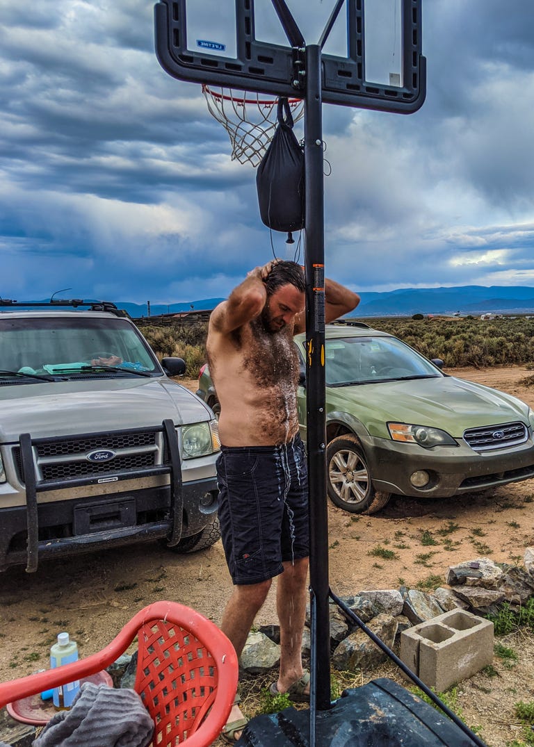The writer showering with water from a bag hanging on a basketball hoop.