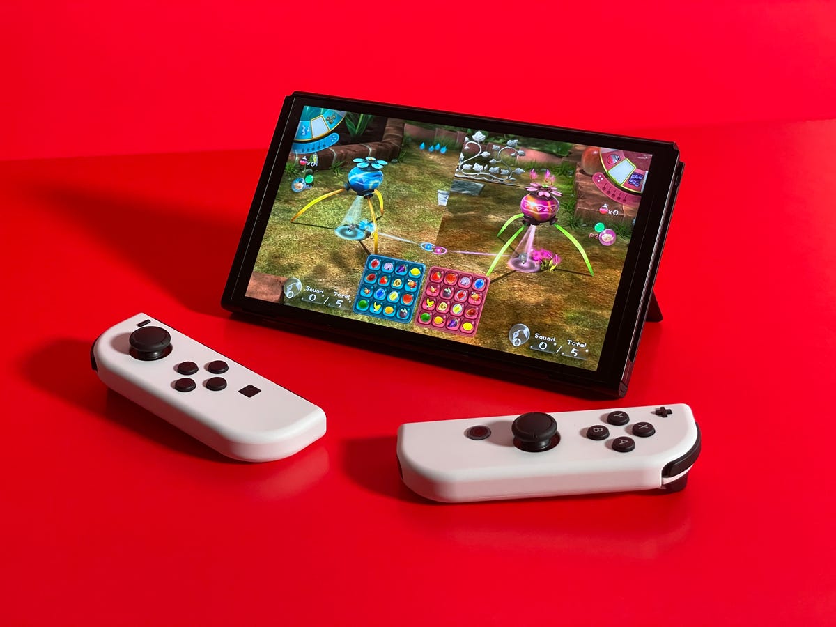 Nintendo Switch OLED with two controllers, and a red background.