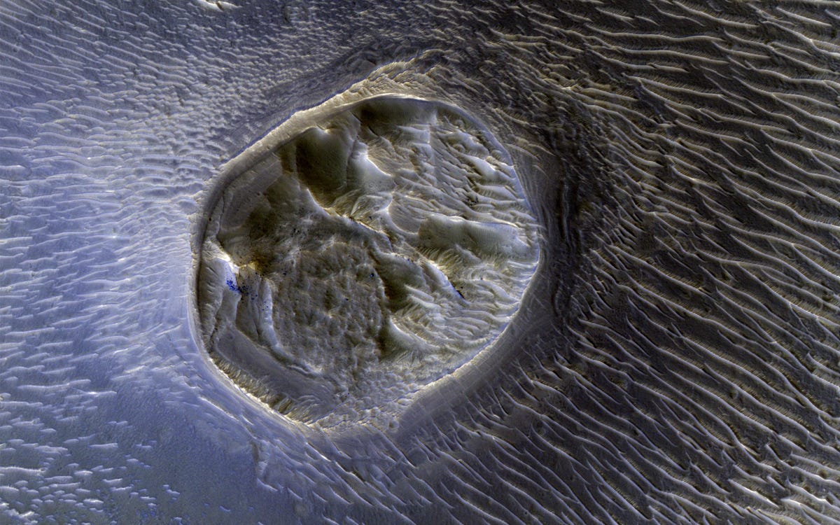 Wavy sand dunes surround roundish, pockmarked Martian mesa.
