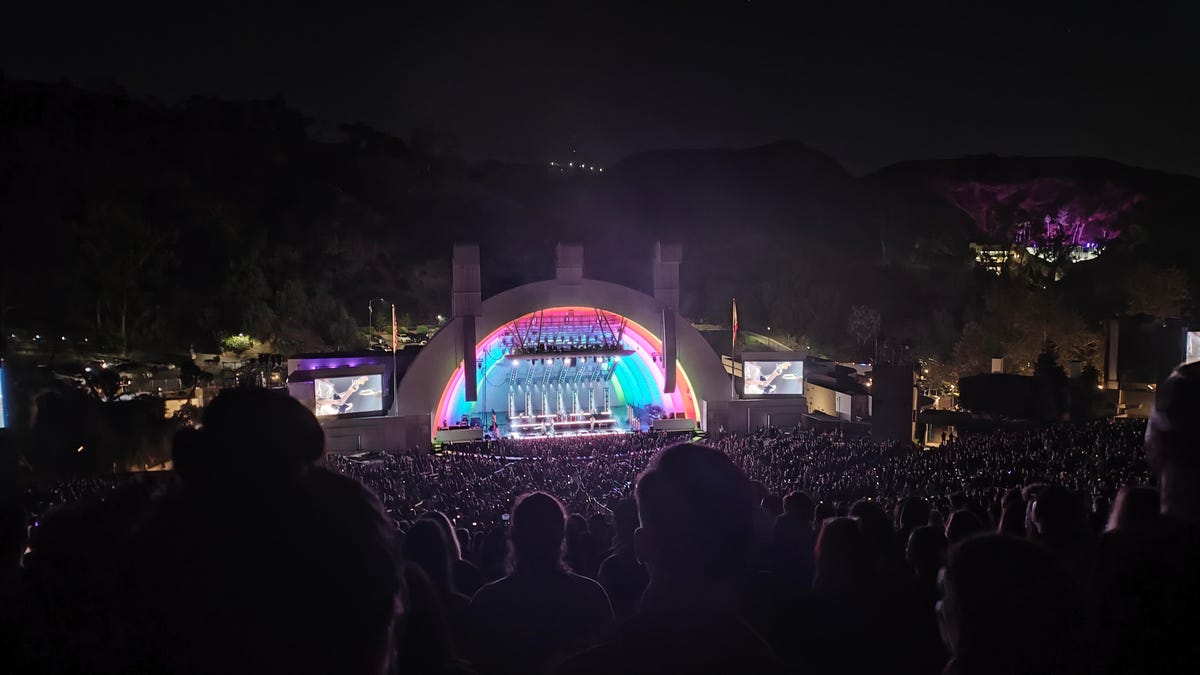 An outdoor nighttime concert at the Hollywood Bowl, with bright light on stage washing over the crowd -- the phone captures light-rimmed people but not the dark hills behind the stage.