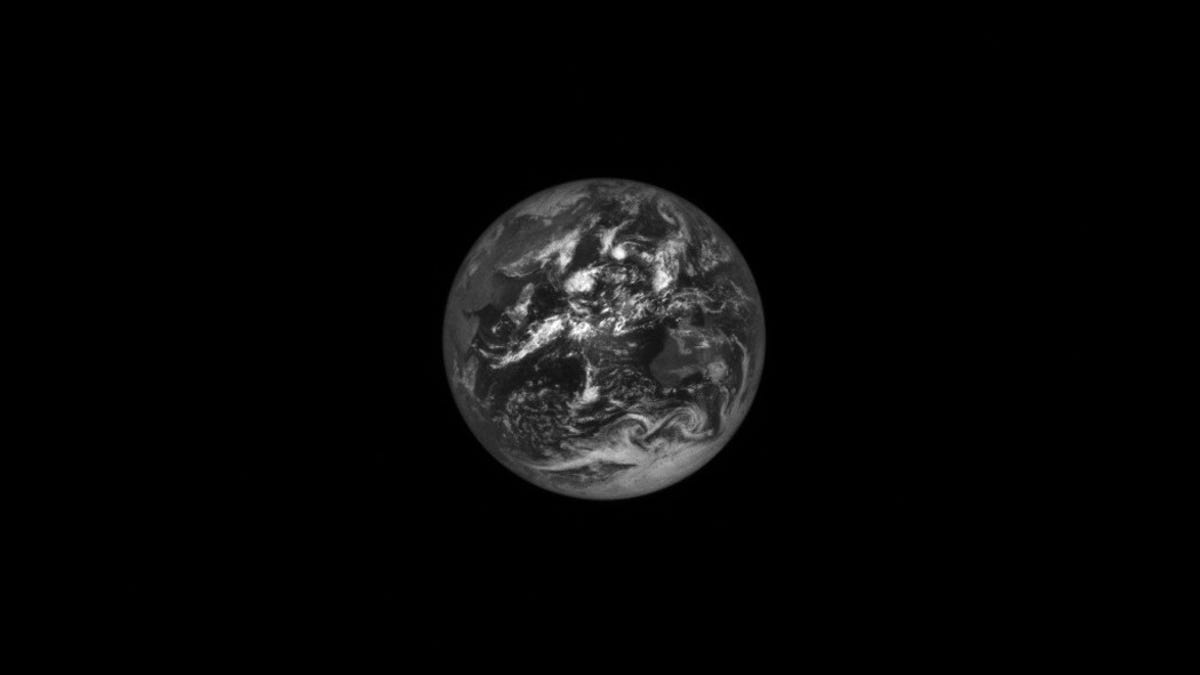 Earth appears as a black-and-white marble against darkness as seen from a distant spacecraft view.