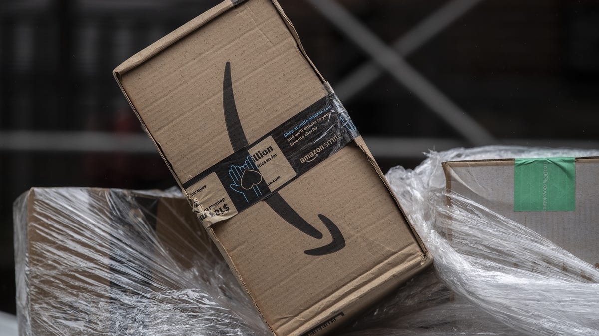 A pile of Amazon boxes with the one on top tipped sideways, showing a tilted Amazon smile logo.