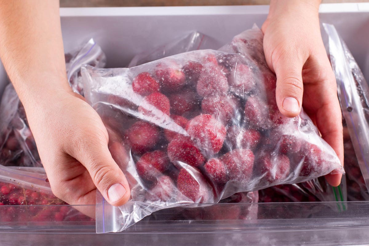 A person handles a bag of frozen strawberries