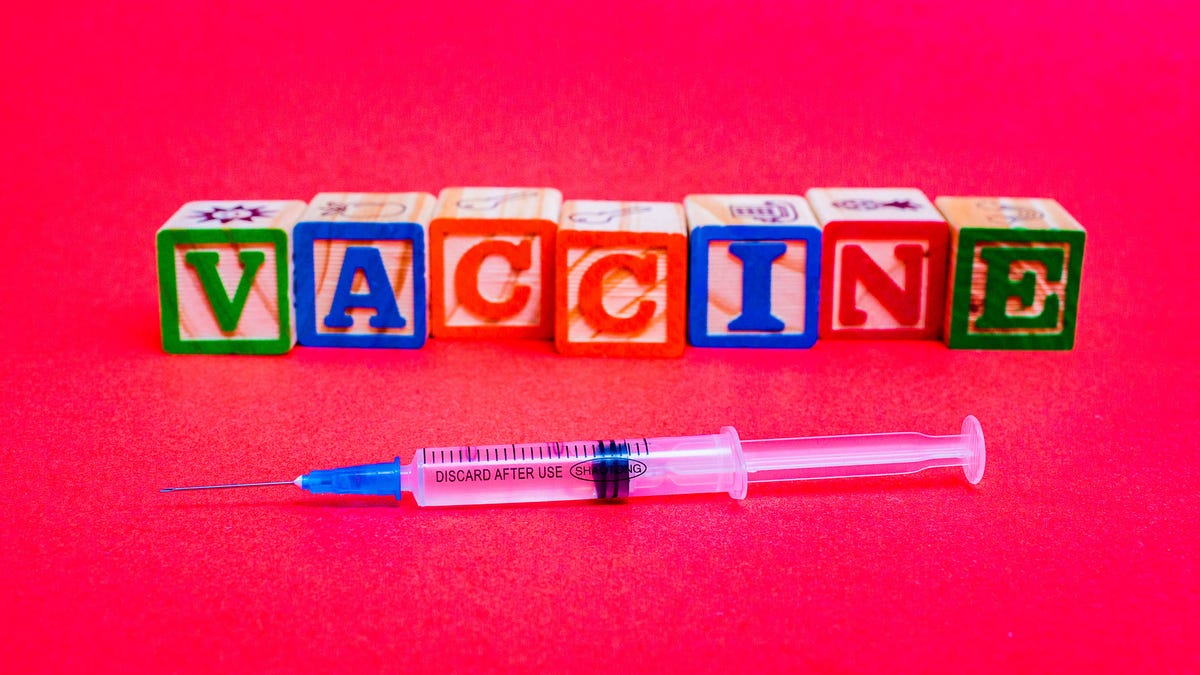 The word "vaccine" spelled out in children's blocks on a bright red background.