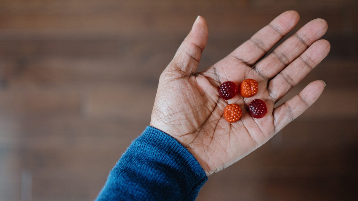 A person holds four orange and red melatonin gummies in the palm of their hand