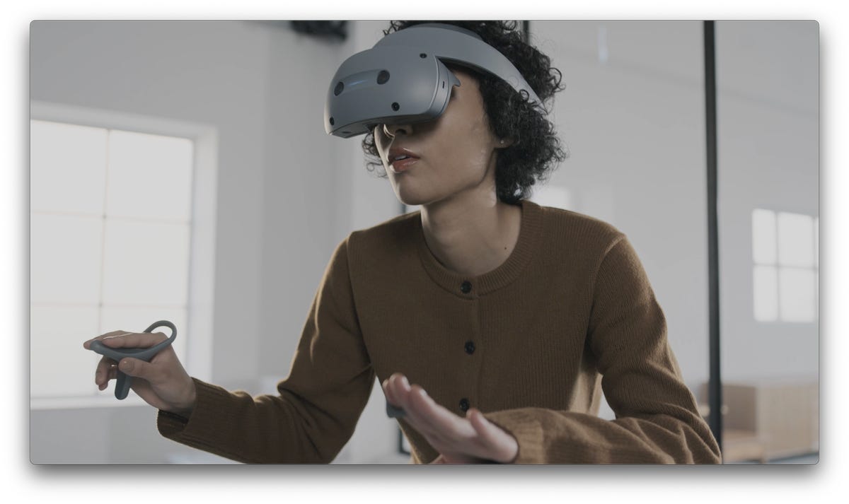 A woman wearing a gray flip-up VR headset with a ring and controller in her hands