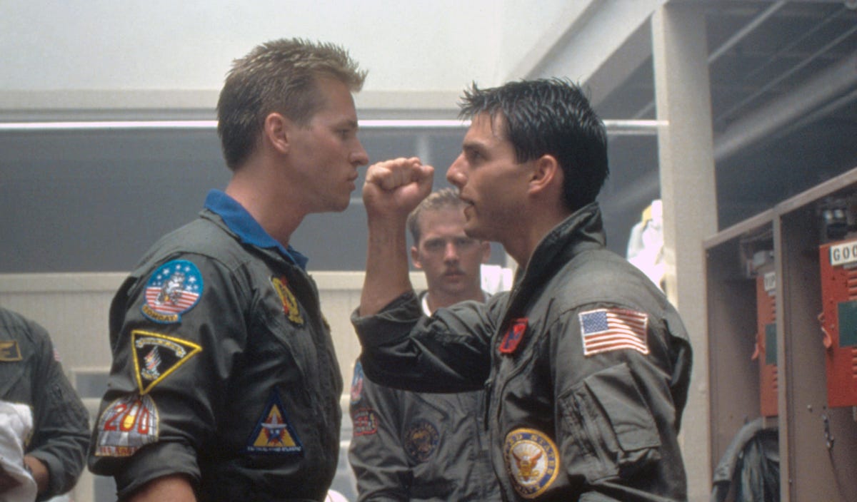 Young Val Kilmer and Tom Cruise argue in military uniform in the originalTop Gun.