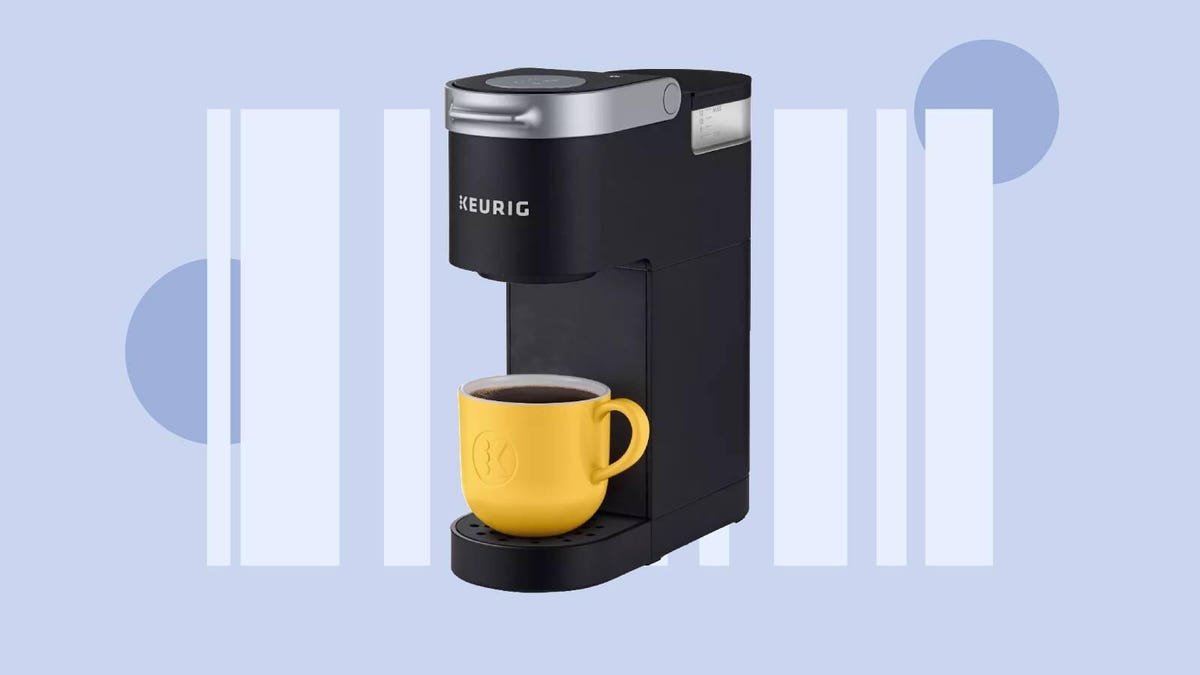 A black Keurig single-serve coffee brewer and a yellow mug against a gray background.