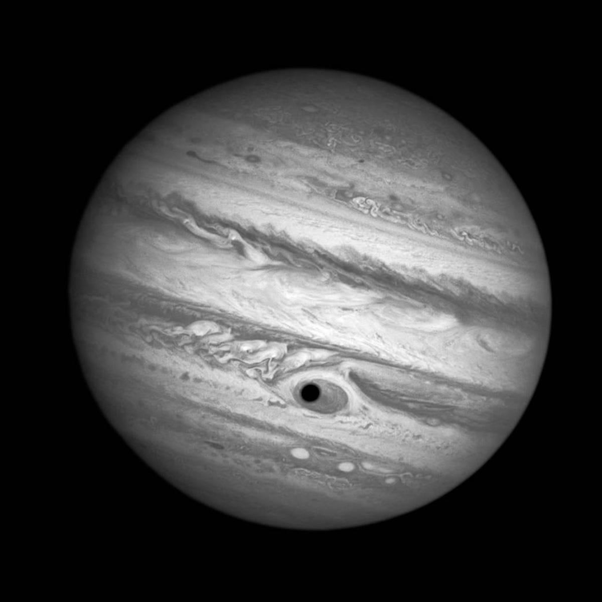 Jupiter in black and white looks like a swirly marble with a dark moon shadow falling on an oval storm, making it look like an eye.