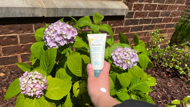 A hand holding Aveeno Mineral Sunscreen
