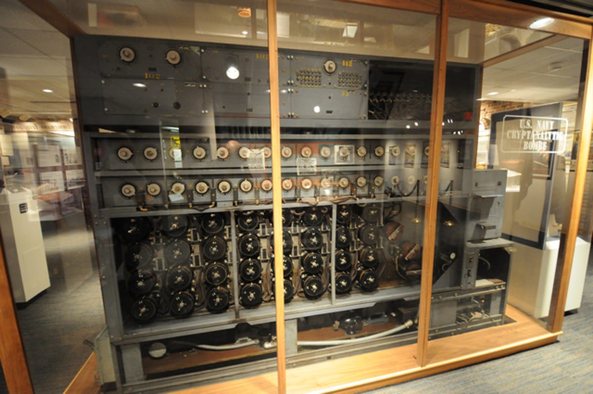 Photograph of a U.S. Navy cryptanalytic bombe, the size of about three large refrigerators side by side, in a glass case. The machines 