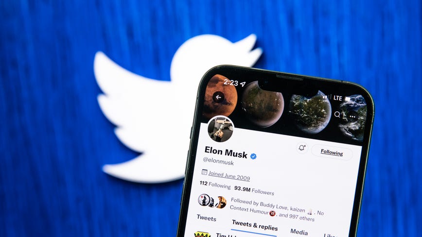 Elon Musk's Twitter account on a mobile phone, in front of a Twitter logo