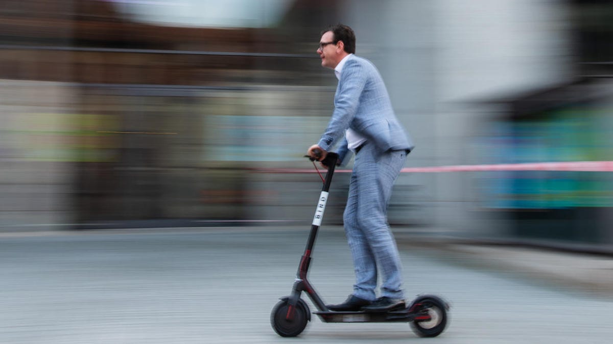 A man zips along on an e-scooter, in front of a motion-blur background
