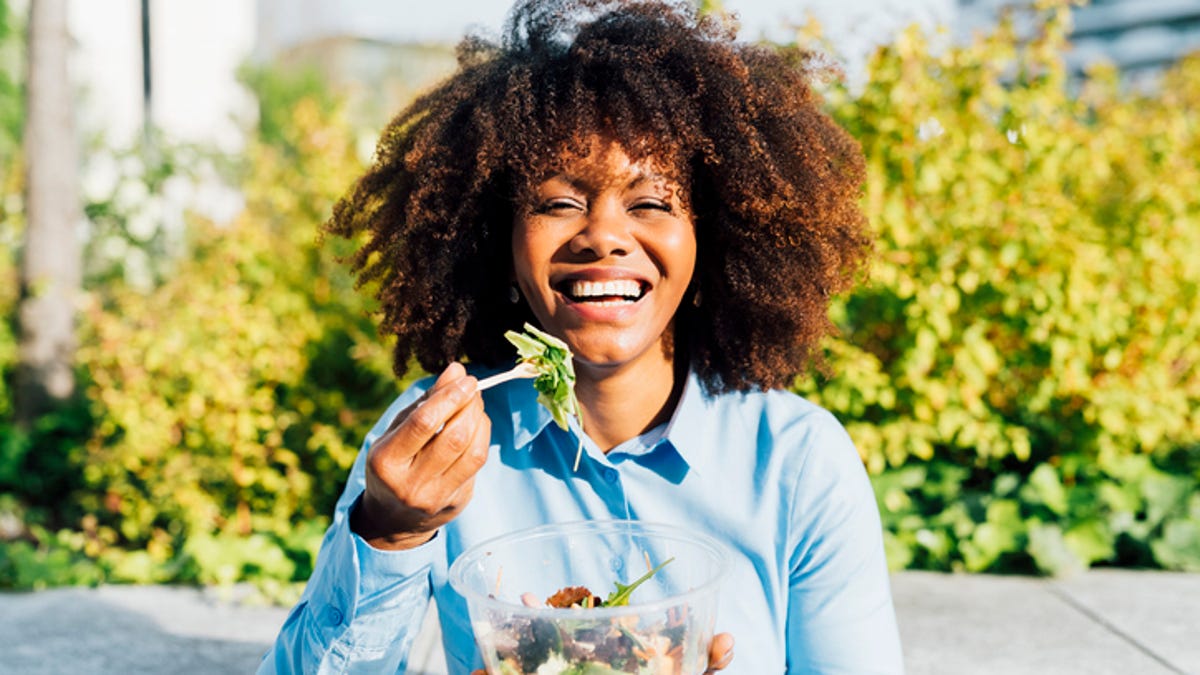 Smiling woman eating a salad outside