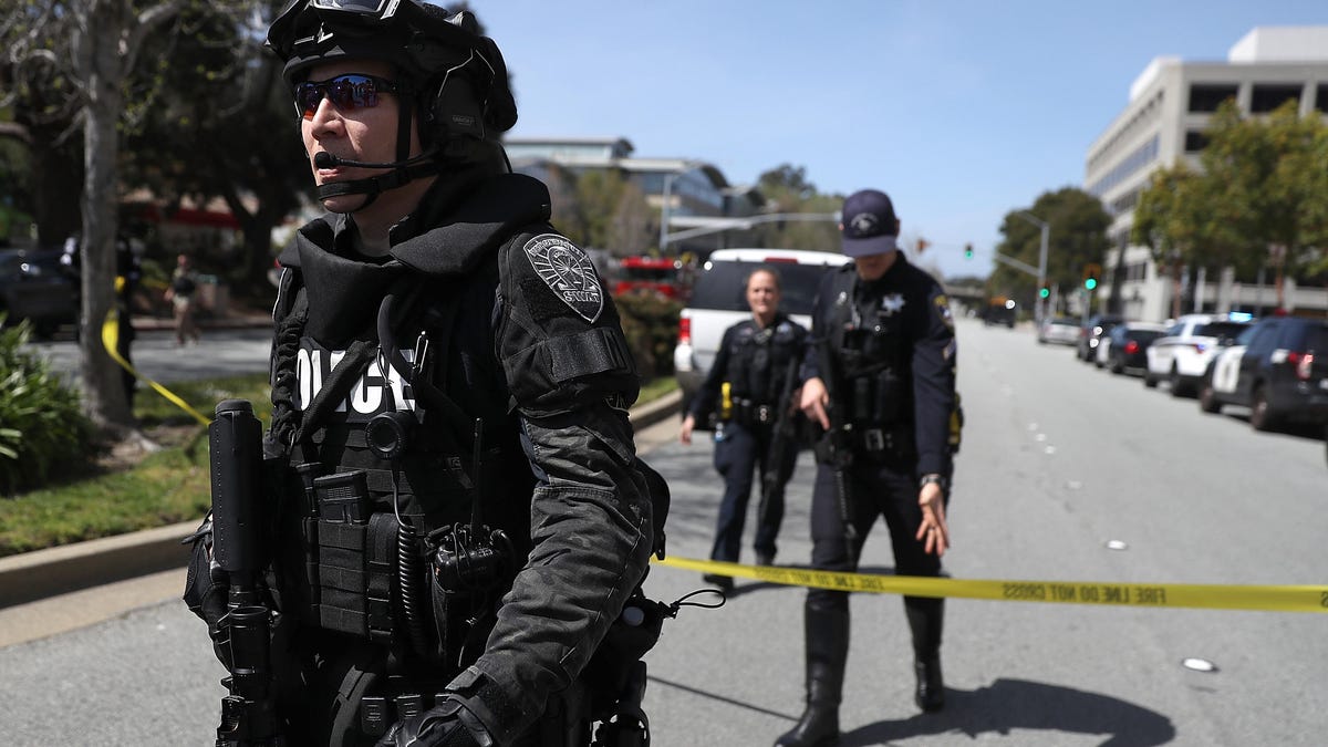 Law enforcement officers cross yellow police tape amid a shooting at YouTube Headquarters In San Bruno, California